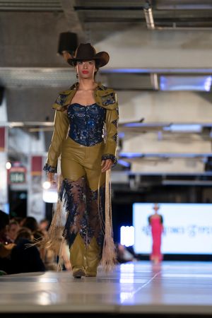 Western-inspired runway look featuring brown leather jacket and navy corset with sheer details.