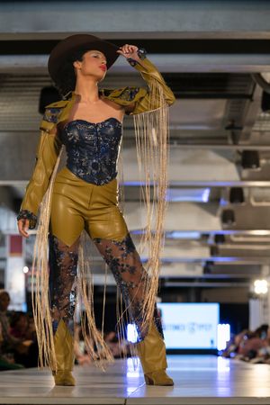 A western-inspired outfit featuring blue lace and gold fringe details on display at a fashion show.