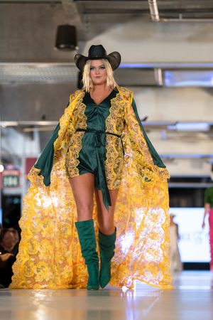 Dramatic yellow cape with green accents flows on fashion runway.