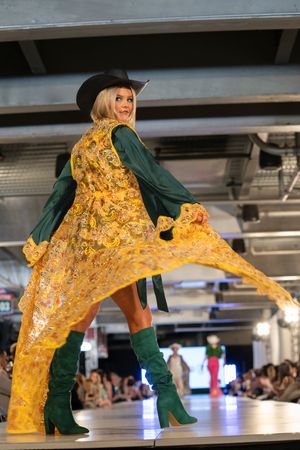 Yellow flowing cape dress with green boots creates dramatic movement on catwalk.