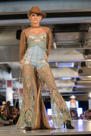 Western-inspired outfit with sheer lace pants and brown hat on fashion catwalk.