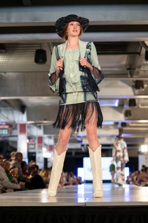 Model presents mint green outfit with black fringe details and white boots.