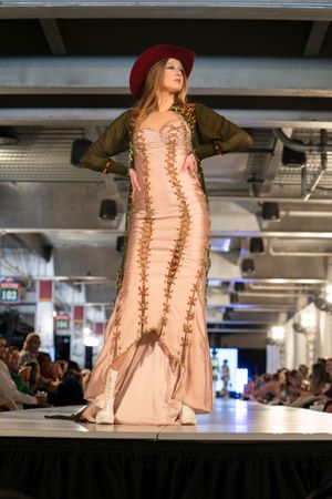 Model showcases vintage-inspired peach dress with lace-up details on runway.
