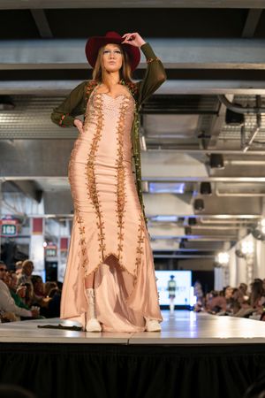 Model presents peach-colored dress with intricate lace detailing on runway.
