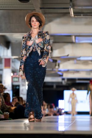 Navy sequined gown with ornate pattern and brown hat styled for western fashion runway show.
