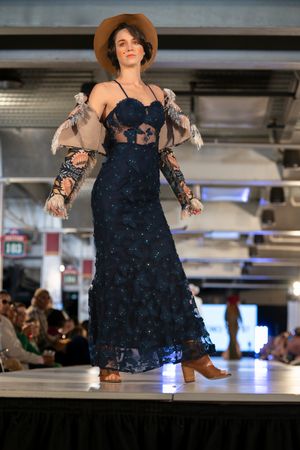 Navy lace gown with dramatic puffy sleeves and brown hat displayed on fashion runway.