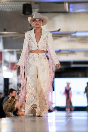 Western-inspired white fringe outfit with cowboy hat featured on fashion runway.