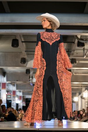 A black dress with coral lace overlay being showcased on a fashion runway.