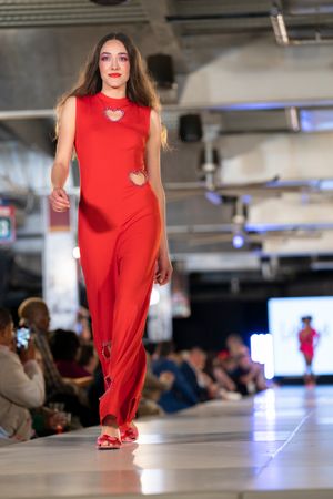 Model presents bright red jumpsuit with cutout details on illuminated runway.