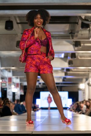 Model walks runway in vibrant red and pink floral print matching shorts and jacket set with red platform shoes.