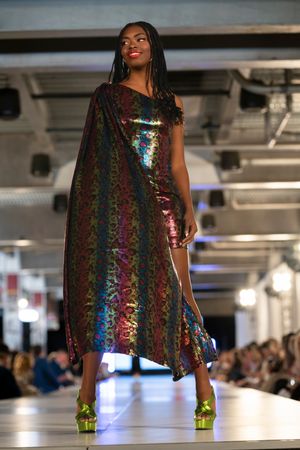 Model struts down catwalk wearing iridescent rainbow sequined dress paired with bright green platform shoes.