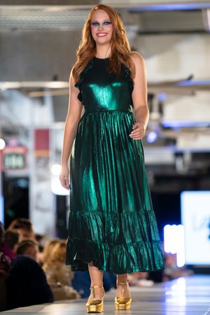 Emerald green metallic maxi dress with tiered skirt presented on runway.