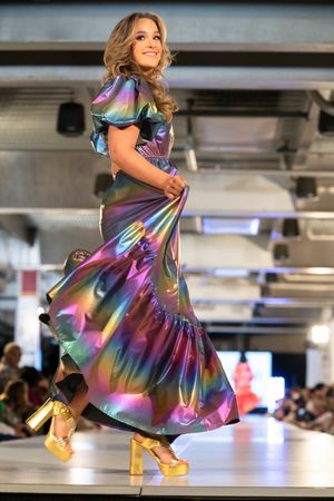 Holographic rainbow dress with metallic finish twirls on runway during fashion show.