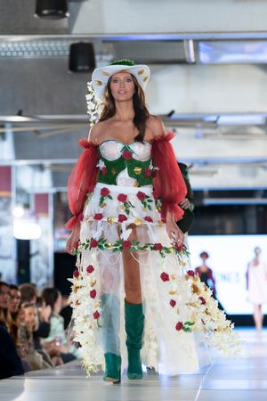 Whimsical white dress with red floral accents and green details shown on fashion runway.