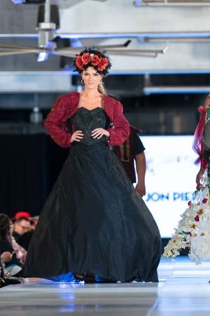 Dramatic black ballgown with red accents and floral headpiece showcased on industrial catwalk.