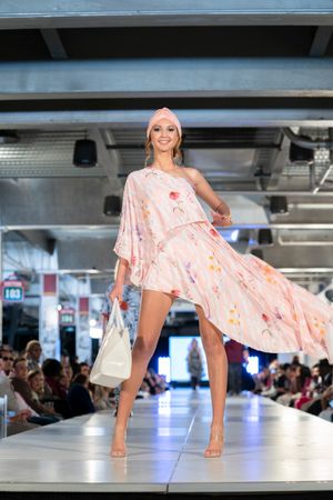 Model twirls in flowing peach floral dress on illuminated runway during fashion show.