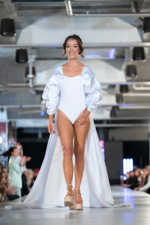 White dramatic coat dress with puffy sleeves shown on illuminated indoor runway.