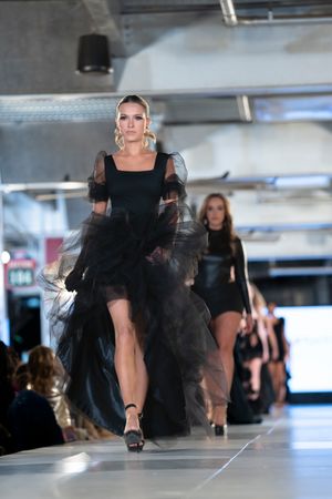 Models showcase dramatic black tulle gowns on illuminated catwalk during fashion event.