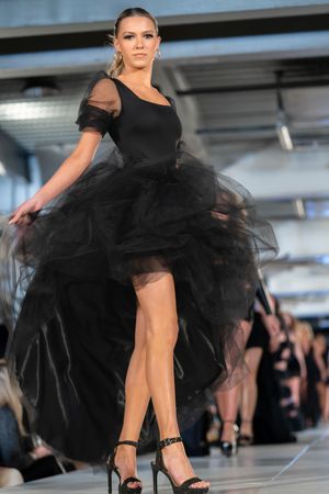 Dramatic black tulle gown with asymmetrical hemline showcased on catwalk.