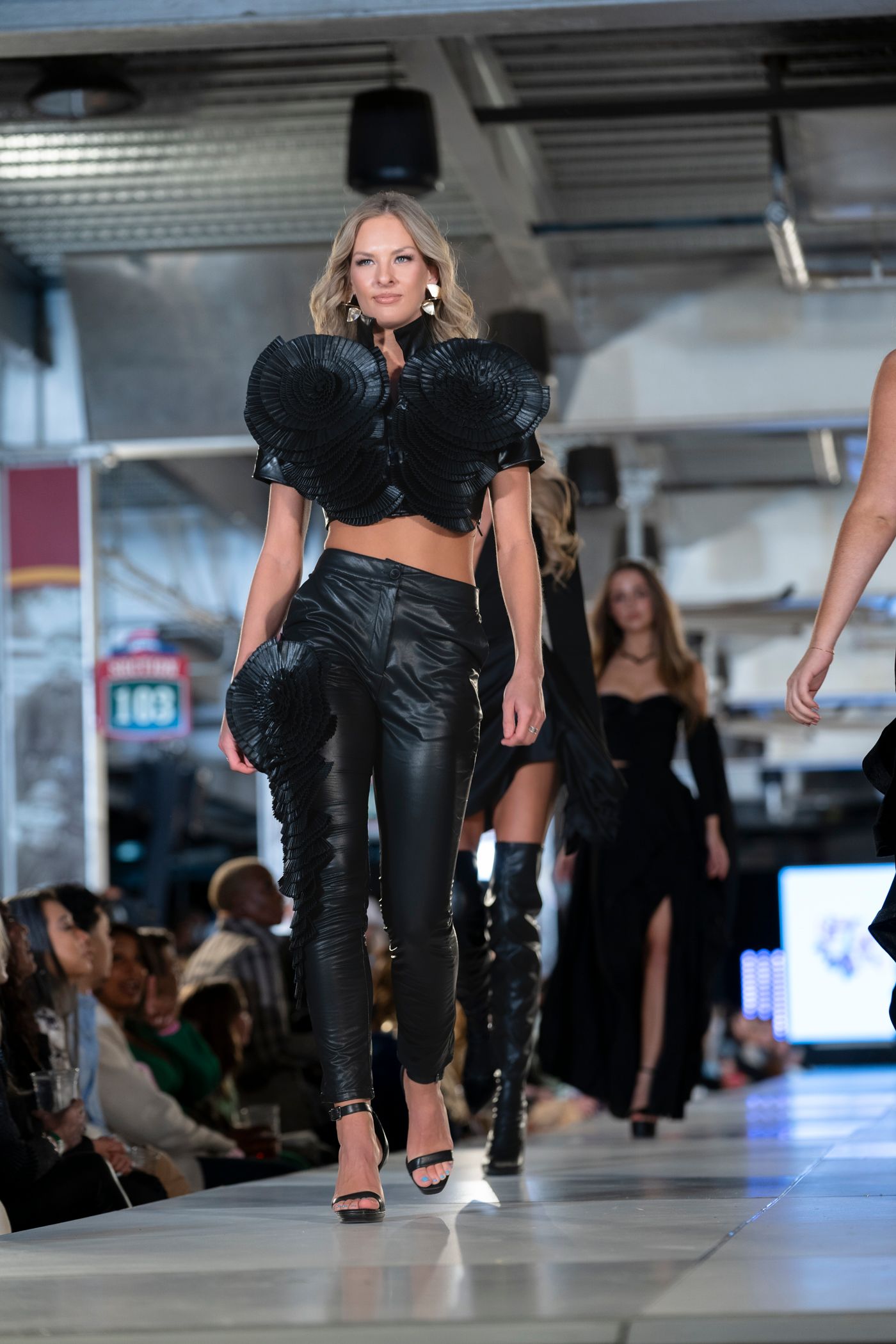 Models walk the runway in black leather outfits during a fashion show event.