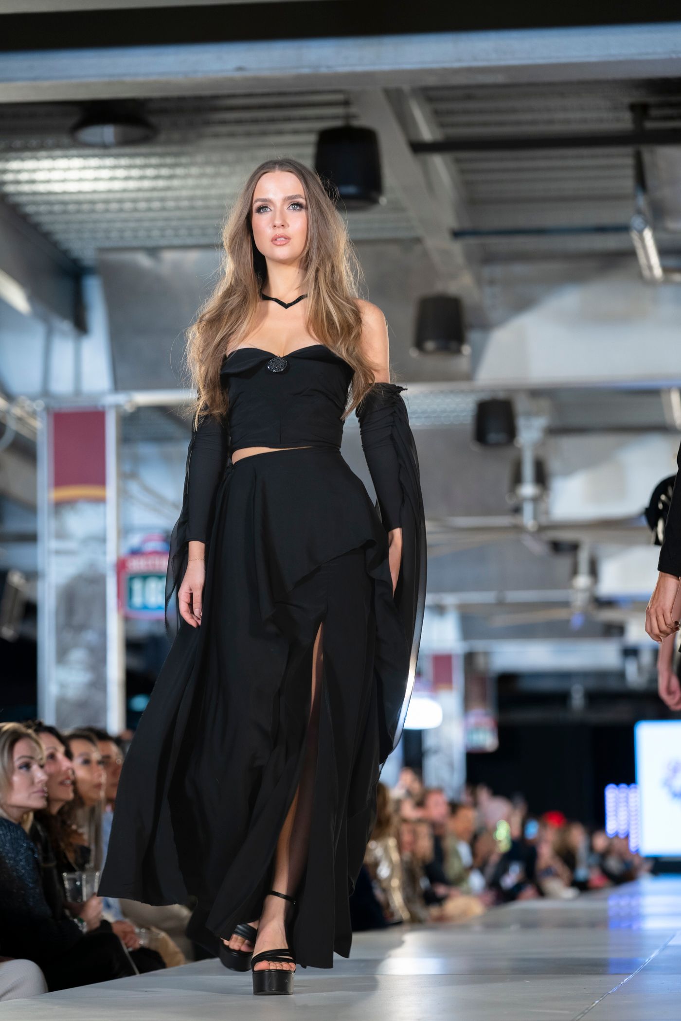 Models showcase elegant black evening wear designs on a modern runway during a high-end fashion show.