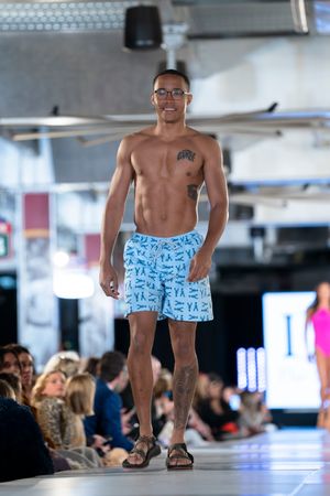 Models showcase swimwear designs on an illuminated runway during a fashion show.