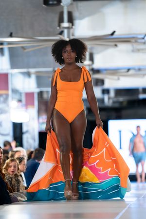 Model presents vibrant orange swimsuit with wave design detail during fashion show.