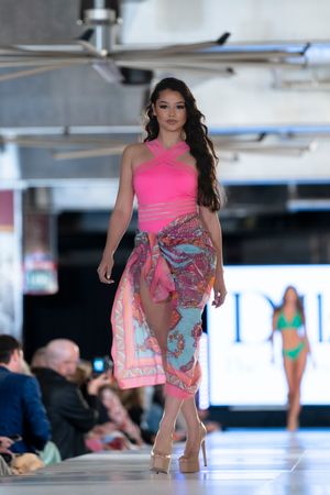 Model showcases colorful pink and blue resort wear on illuminated catwalk.