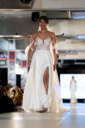 Elegant white wedding gown with corset bodice and flowing skirt displayed on fashion runway.