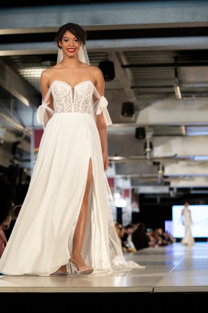 Elegant white wedding dresses with lace details presented at a runway fashion show.