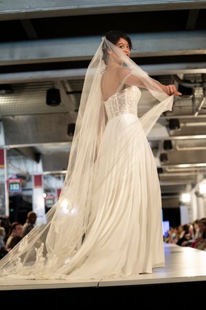 Bridal fashion show featuring flowing white wedding gown with dramatic veil on runway.
