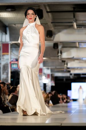 Model showcases flowing white satin gown on illuminated catwalk.