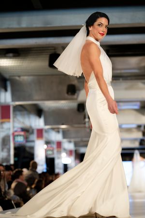 A stunning fitted white wedding gown with a low back and flowing train shown on a fashion runway.