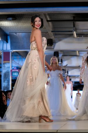 Strapless wedding dress with floral appliques shown on illuminated catwalk.