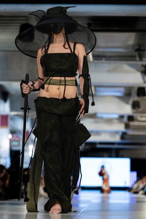 Dramatic black ensemble with wide-brimmed hat and crop top on fashion runway.