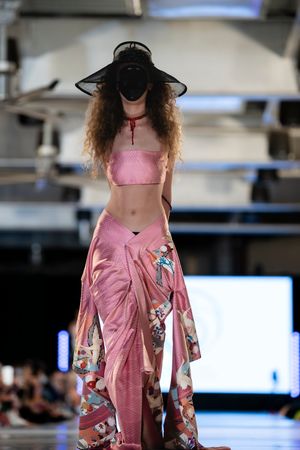 Pink crop top and flowing floral pants paired with wide-brimmed black hat on runway.