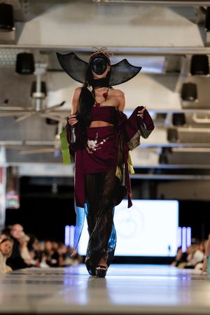Gothic-inspired runway look featuring dramatic bat-wing headpiece and burgundy ensemble.