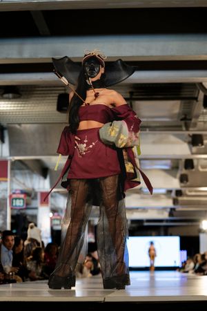 Model presents burgundy and black sheer lingerie ensemble on illuminated catwalk.
