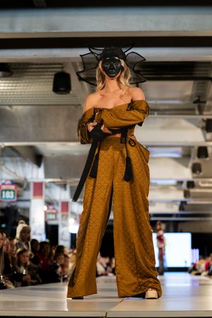 Catwalk model presents flowing brown gown with dramatic sleeves in modern venue setting.