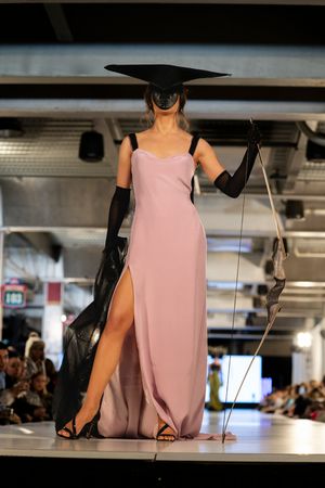 Model presents elegant pink slip dress with black accessories and dramatic wide-brimmed hat.
