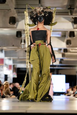 Avant-garde runway look featuring olive pants, black top, and dramatic gold wing accessories.