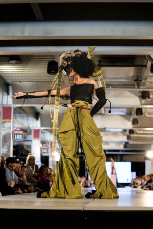 Dramatic olive green wide-leg pants with black top shown on fashion runway.