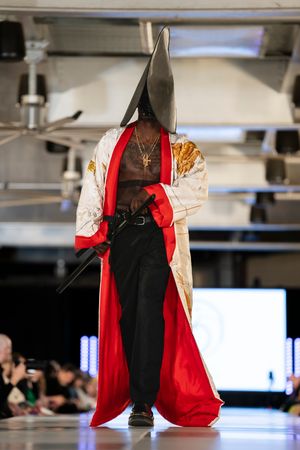 Model showcases dramatic black and red cape ensemble on fashion runway.