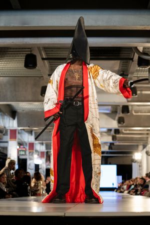 Fashion models showcase dramatic black and red outfits with flowing fabrics on an indoor runway.
