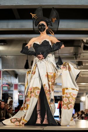An avant-garde white and gold printed dress with dramatic black accents shown on a fashion runway.