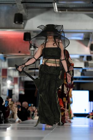 Models present dramatic black evening wear collection on illuminated catwalk.