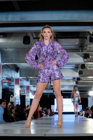 Purple ruffled mini dress design presented on illuminated runway.