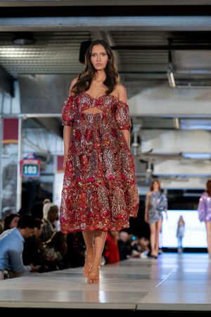 Flowing red floral off-shoulder midi dress displayed at indoor fashion show.