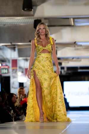 Flowing yellow gown with floral details presented on illuminated catwalk.