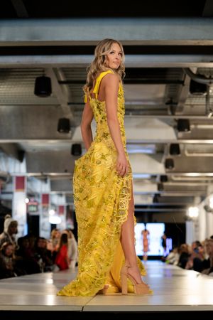Model presents flowing yellow lace dress with side slit on fashion runway.